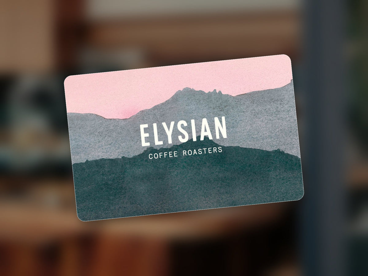 Elysian in-store gift card with the painted mountain design, in front of a blurred cafe