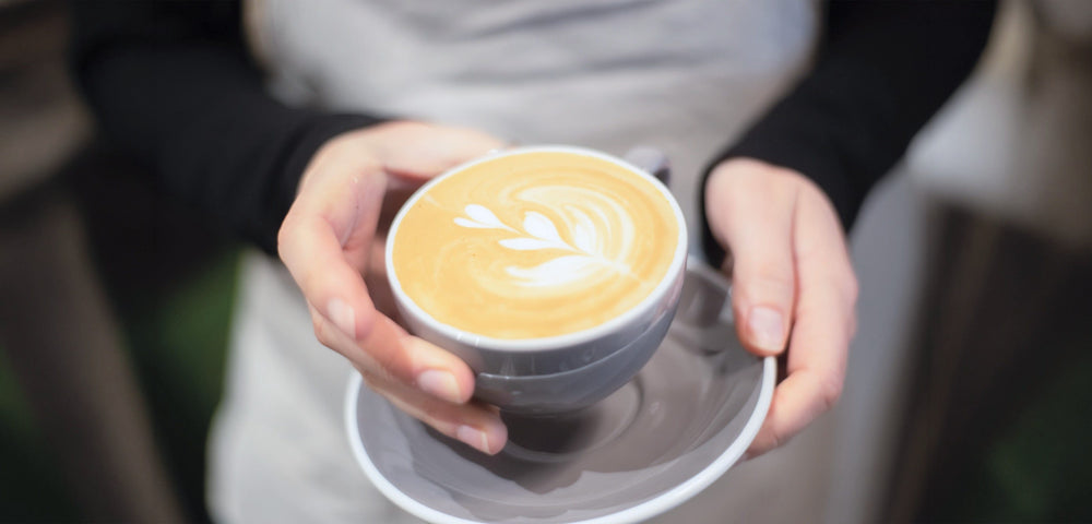 Hands holding a latte with leaf latte art