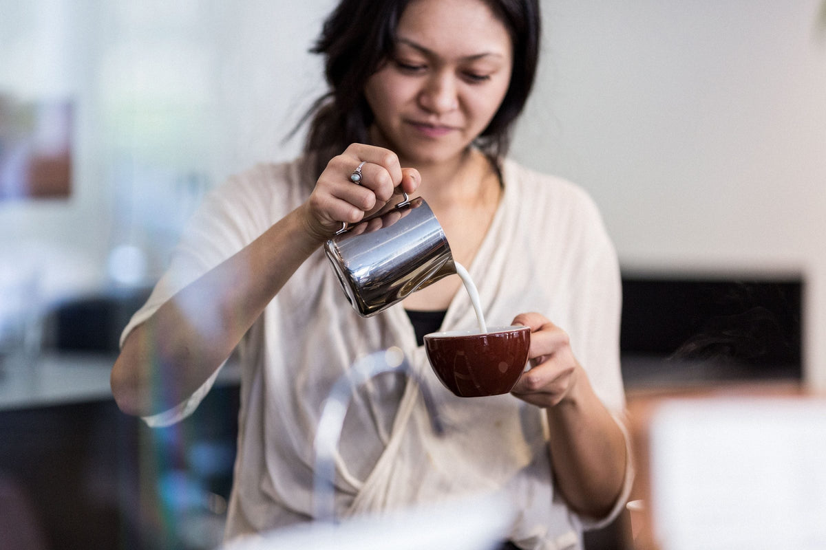 An Elysian barista pouring milk into a cappuccino